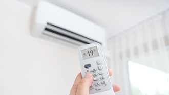 Mão com comando de ar condicionado a mostrar 19ºC no visor e a apontar para aparelho de ar condicionado na parede.